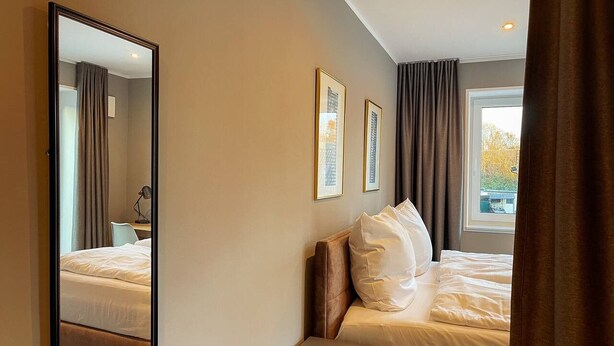 Quarto de hotel com cama, mesa de cabeceira, espelho e janela com cortinas.