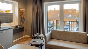Sala de estar moderna com sofá, mesa pequena, TV e varanda com vista para edifícios.