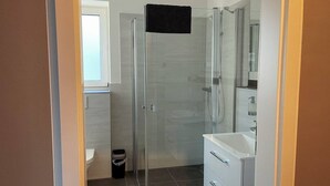 Uma casa de banho moderna com cabine de duche em vidro, lavatório branco e espelho.