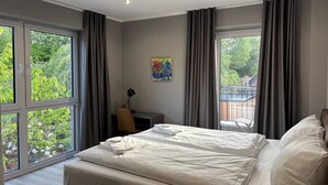 Quarto moderno com uma cama grande, uma escrivaninha e vista para o verde lá fora.