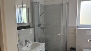 Casa de banho moderna com chuveiro em cabine de vidro, lavatório branco e sanita.