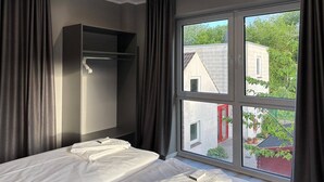 Quarto de hotel com cama, guarda-roupa e uma janela ampla com vista para edifícios e áreas verdes.