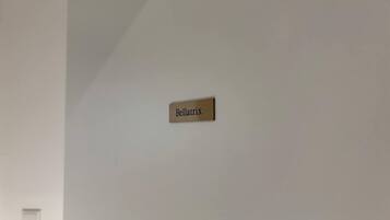 Une enseigne fixée au mur, portant le nom « Bellatrix », dans une pièce aux murs blancs, où l’on aperçoit un unique interrupteur sur le côté gauche.