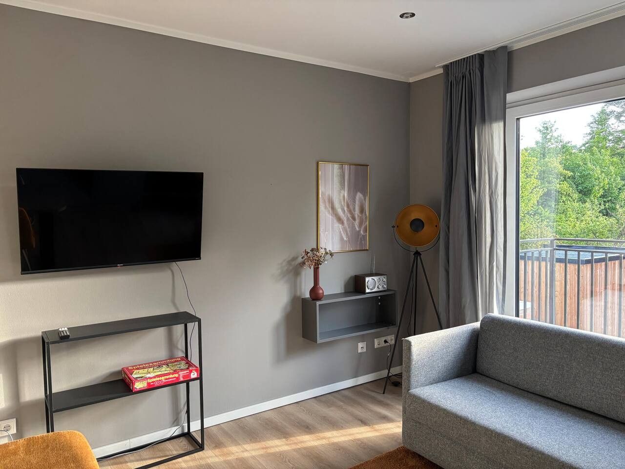 A modern living room with a flat-screen TV, a grey sofa, a console table with a vase, and a floor lamp.