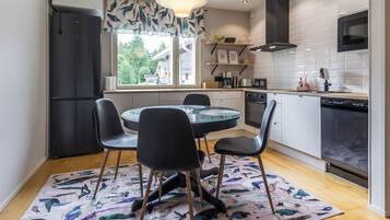 Une cuisine moderne avec un coin repas, comprenant une table ronde en verre, des chaises noires, un tapis à motifs et une vue sur l’extérieur.