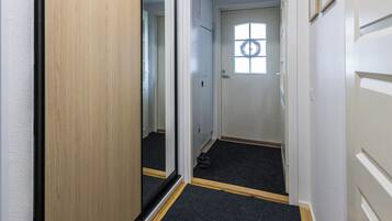 Un pasillo estrecho con piso alfombrado, una puerta con ventanal y el reflejo del pasillo.