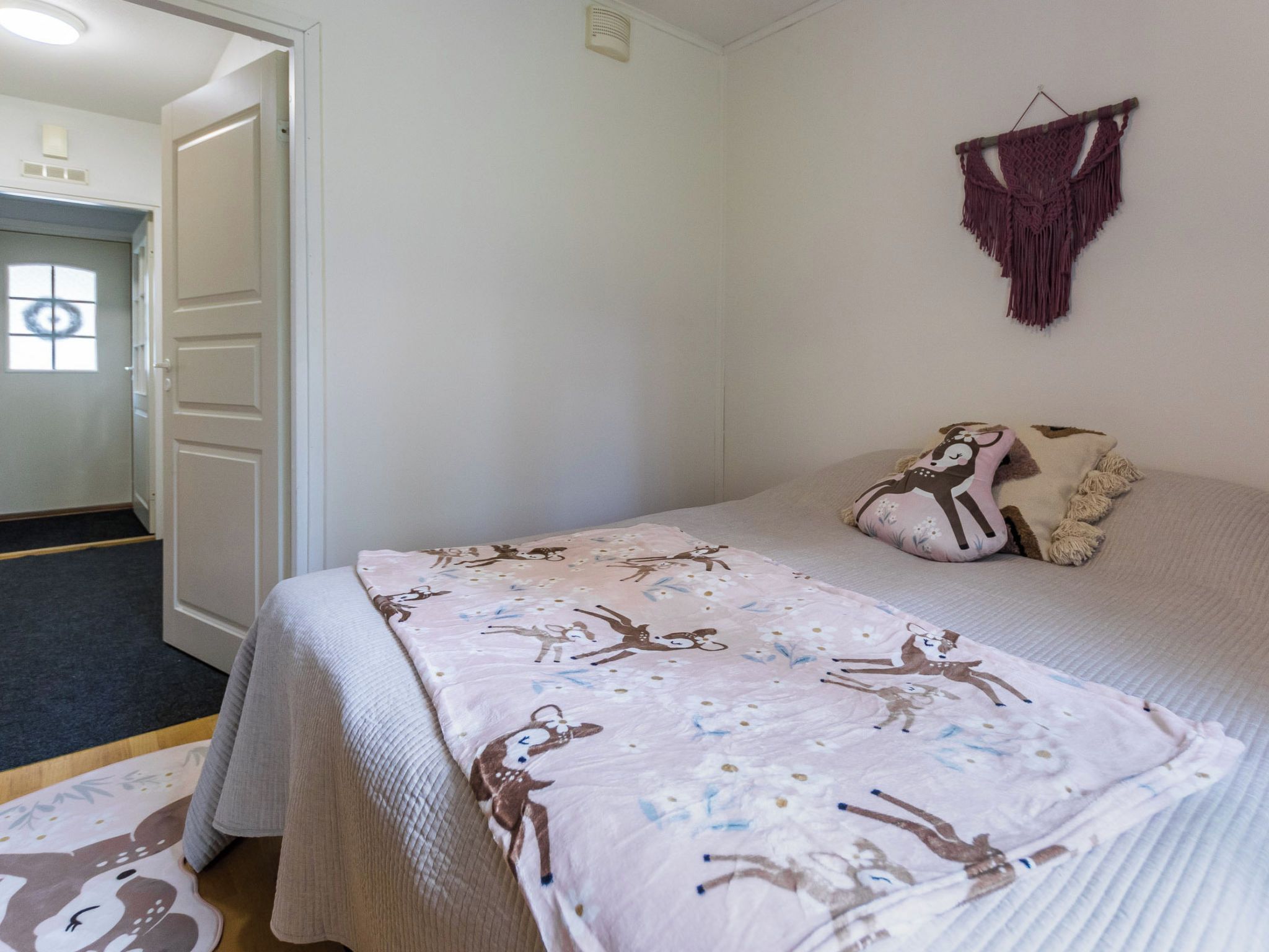 Un dormitorio con una cama, una puerta, un macramé colgado en la pared y una alfombra estampada.