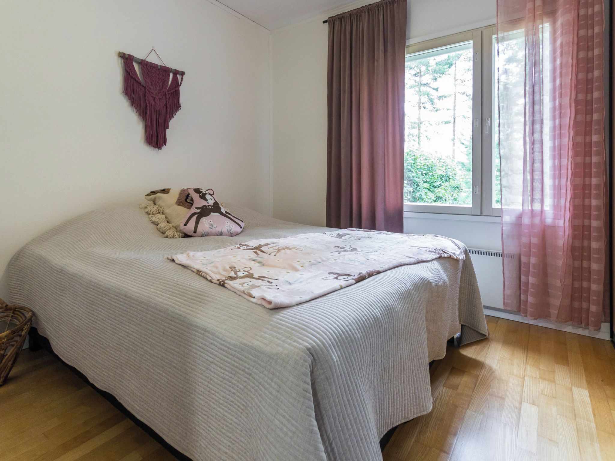 Ein Schlafzimmer mit einem Bett, einem Fenster mit Vorhängen und einer Wanddekoration aus Makramee.