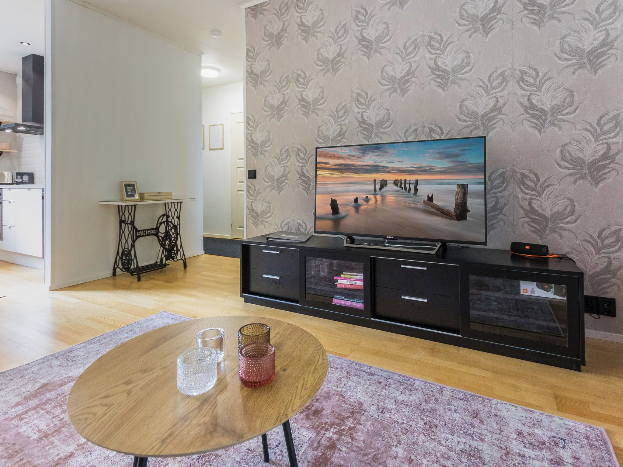 A modern living room with a flat-screen TV, a wooden coffee table, and a patterned rug.