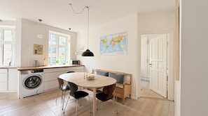 Eine kompakte Küche mit Waschmaschine, einem Esstisch mit Stühlen, einer Karte an der Wand und einer Tür zu einem anderen Raum.