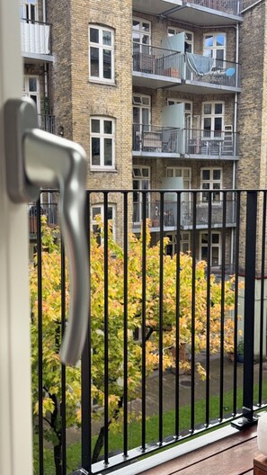 Blick von einem Balkon mit Metallgeländer auf ein Backsteingebäude mit mehreren Fenstern und Balkonen.