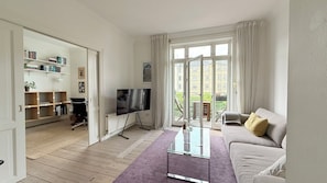 Ein Wohnzimmer mit einer Couch, einem Fernseher, einem Glastisch und einem Bücherregal.