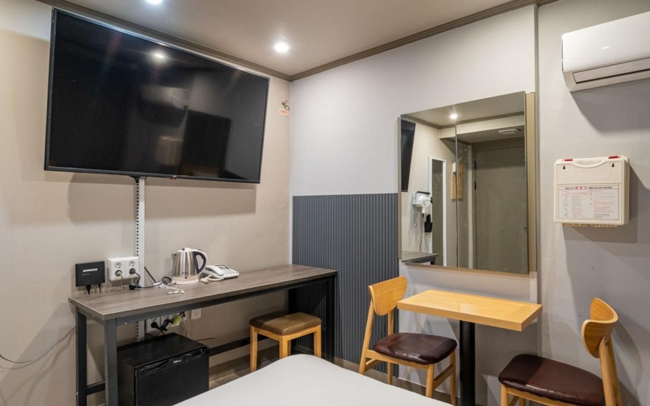Habitación de hotel con una cama, un escritorio con teléfono, una silla, televisor montado en la pared y un espejo.