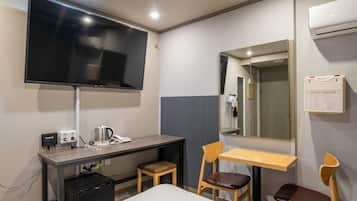 Habitación de hotel con una cama, un escritorio con teléfono, una silla, televisor montado en la pared y un espejo.