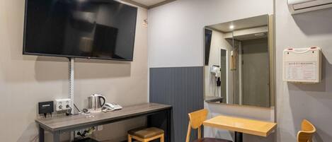 Ett hotellrum med en säng, ett skrivbord med en telefon, en stol, en tv som är monterad på väggen och en spegel.