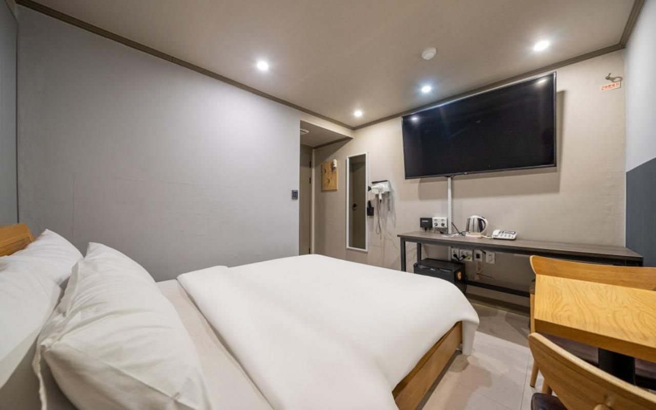 A hotel room with a bed, a desk, a chair, a flat-screen TV, and a wall-mounted phone.