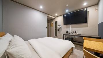 A hotel room with a bed, a desk, a chair, a flat-screen TV, and a wall-mounted phone.
