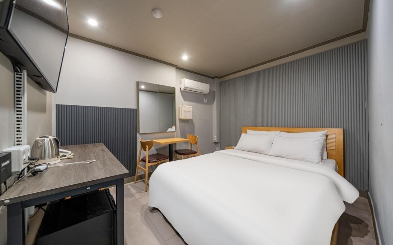 A hotel room with a bed, a desk, a chair, a television, and an air conditioning unit.