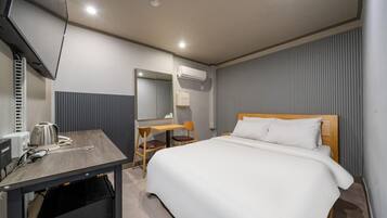 A hotel room with a bed, a desk, a chair, a television, and an air conditioning unit.
