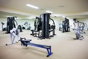 Ein Fitnessraum mit verschiedenen Trainingsgeräten, darunter ein Rudergerät, eine Beinpresse und ein Ergometer.