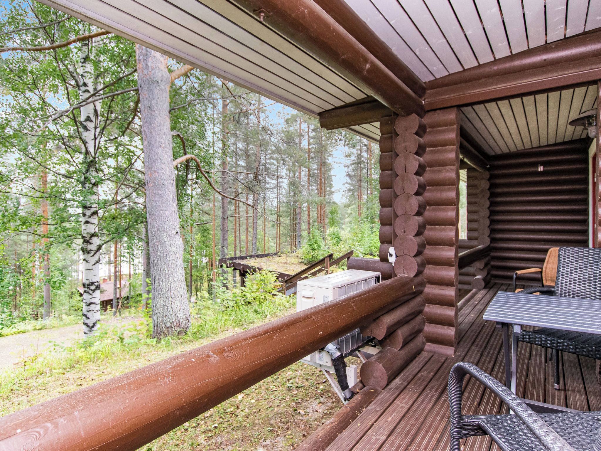 Eine Holzhütte mit überdachter Veranda, Tisch und Stühlen sowie Blick auf den umliegenden Wald.