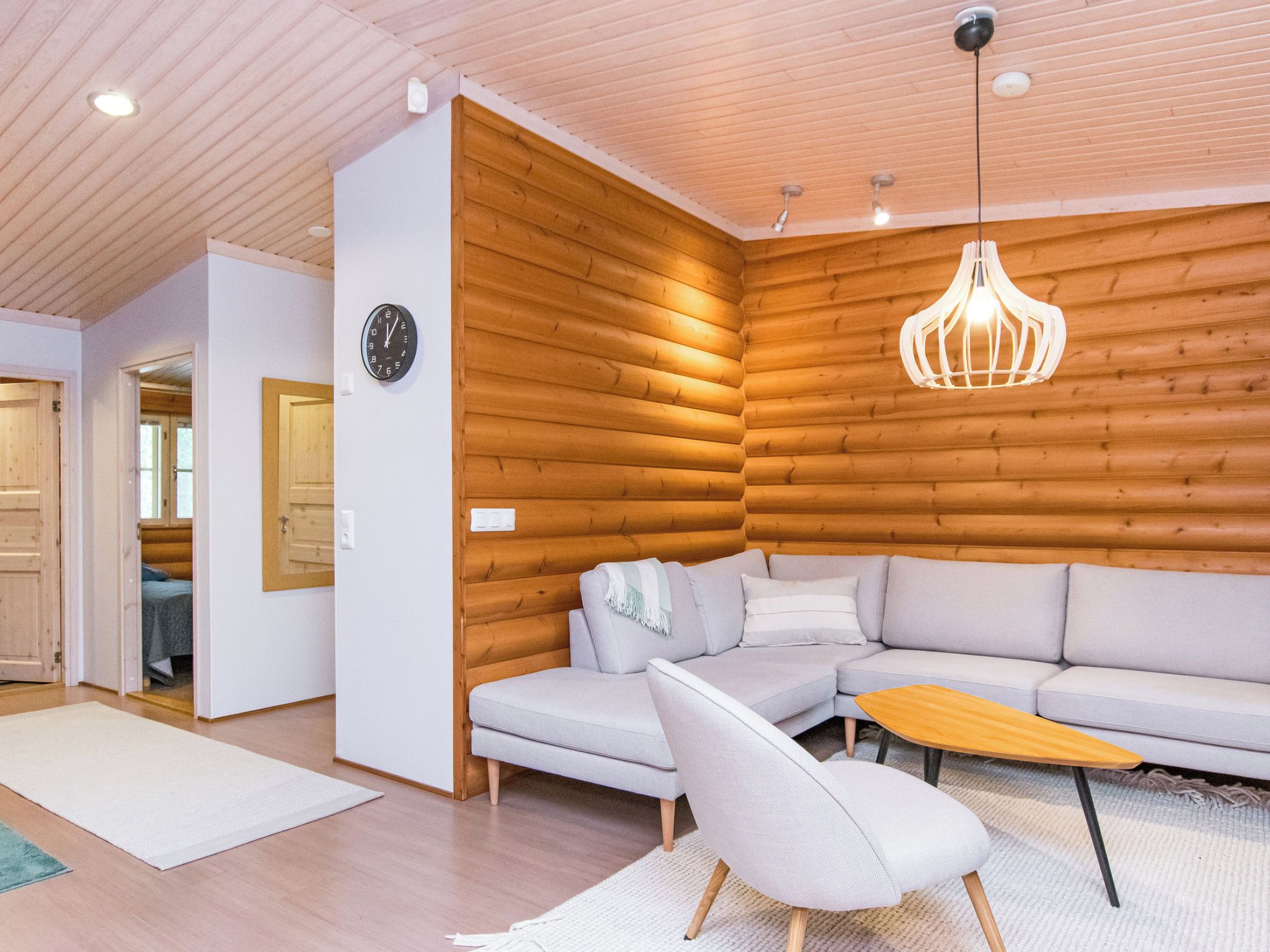 A modern living room with a wooden wall, a sofa, a chair, and a hanging light fixture.
