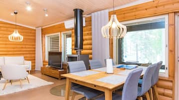 A modern log cabin interior with a dining area, seating, a television, and a fireplace.