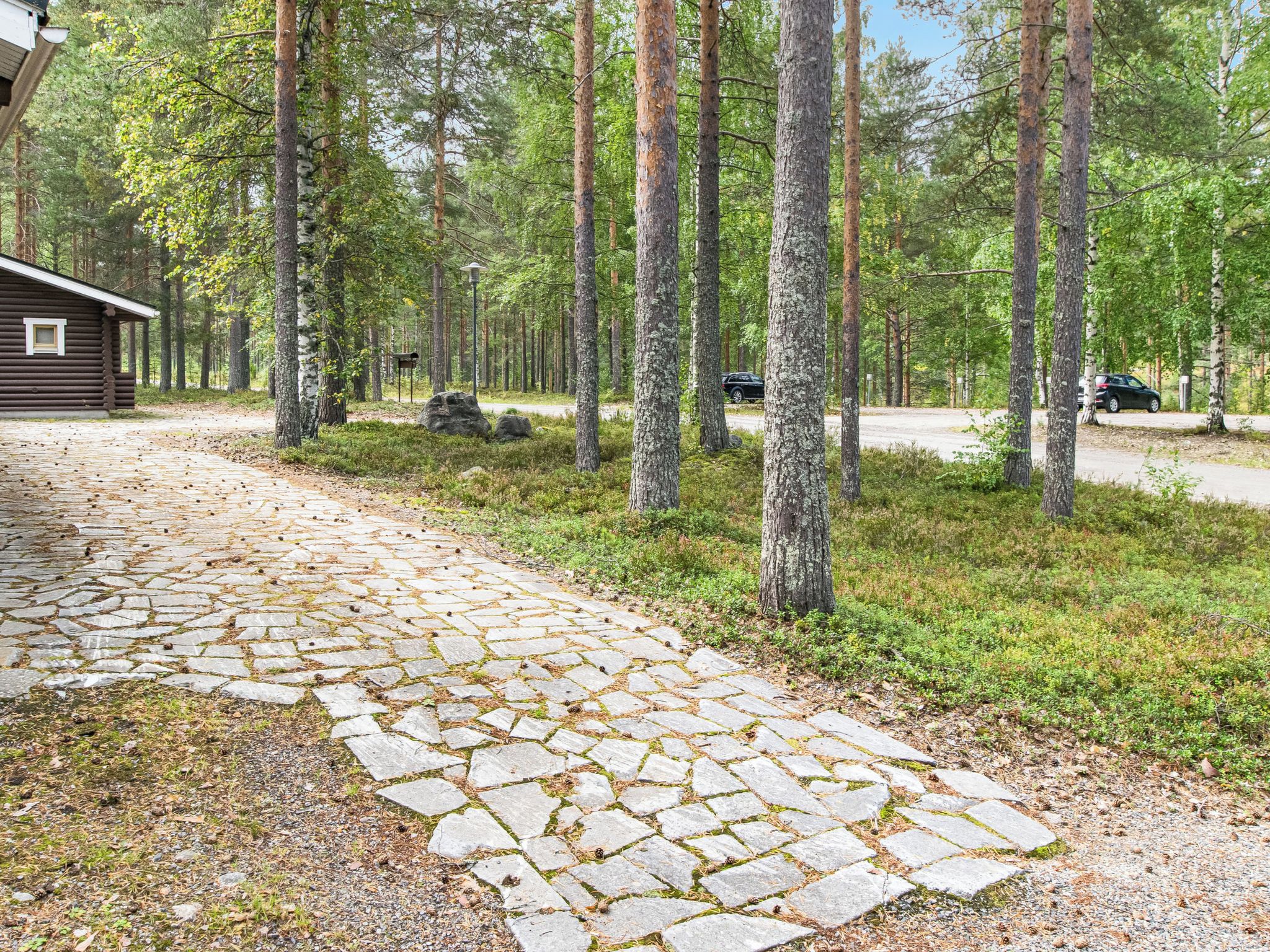 A stone pathway leading to a cabin in a forested area with tall trees and a clear sky.
