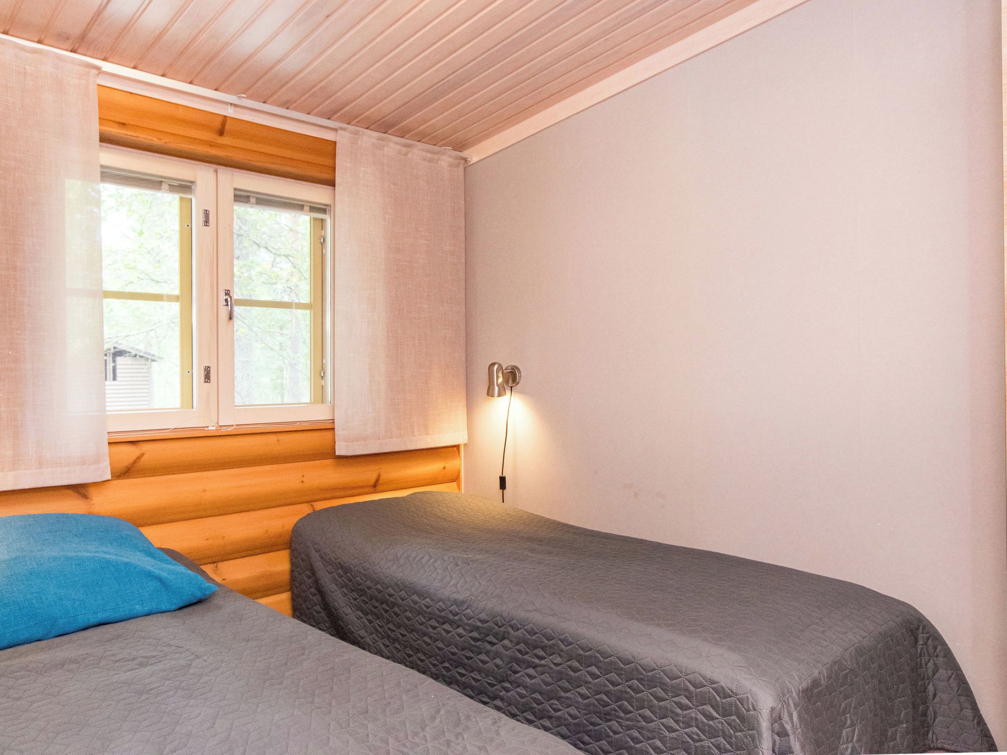 A room with two beds, a window with curtains, and a wall-mounted light.