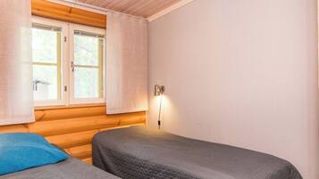 A room with two beds, a window with curtains, and a wall-mounted light.