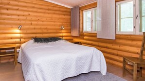 Hirsihuone, jossa on suuri sänky, kaksi yöpöytälamppua ja ikkuna, jossa on sälekaihtimet.