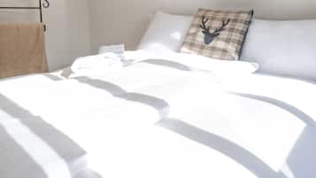 Ein ordentlich bezogenes Bett mit weißen Leinentüchern, ein Kissen mit Karo-Muster und einem Hirsch-Design, sowie ein Metallbettgestell.
