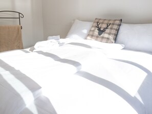 Un lit bien fait, avec du linge de lit blanc, un coussin à carreaux orné d’une tête de cerf et un cadre de lit en métal.
