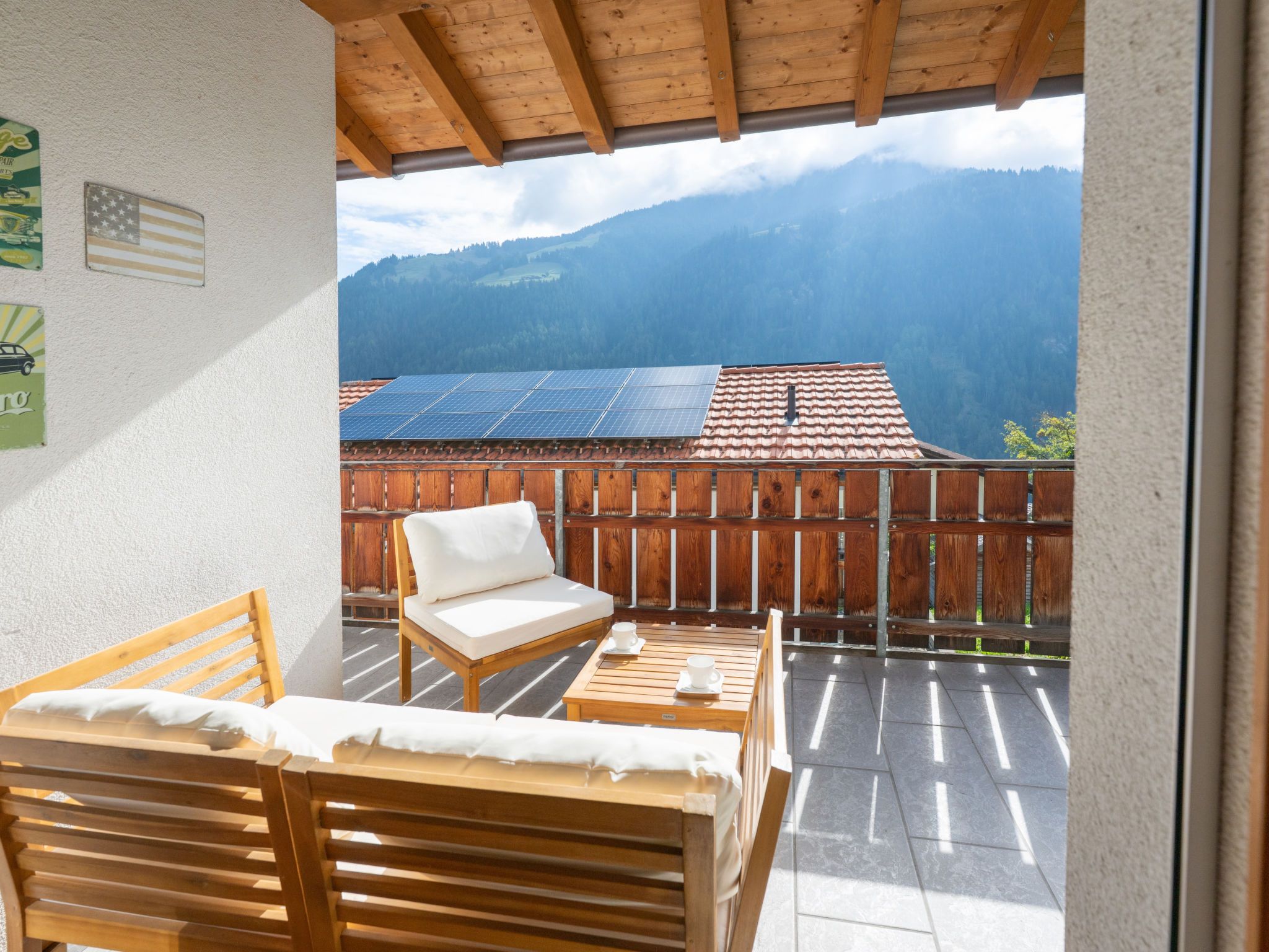 Ein Balkon mit einer Holzbank, einem weißen Sofa und einem Tisch mit Tassen. Auf dem Dach sind Solaranlagen zu sehen.