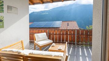 Ein Balkon mit einer Holzbank, einem weißen Sofa und einem Tisch mit Tassen. Auf dem Dach sind Solaranlagen zu sehen.