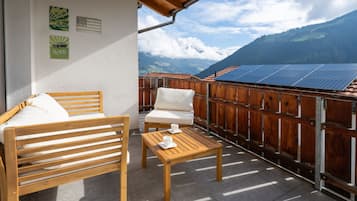 Un balcon avec un banc en bois, une petite table et une vue sur des panneaux solaires et des montagnes.