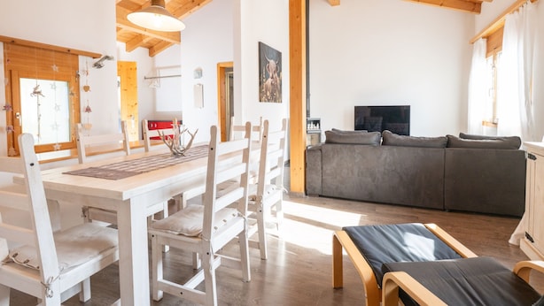 Een ruime woonkamer met een houten plafond, een eettafel met stoelen, een bank en een televisie.