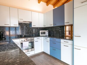 Une cuisine moderne avec des meubles blancs et bleus, un four à micro-ondes, une cuisinière et un plafond en bois.