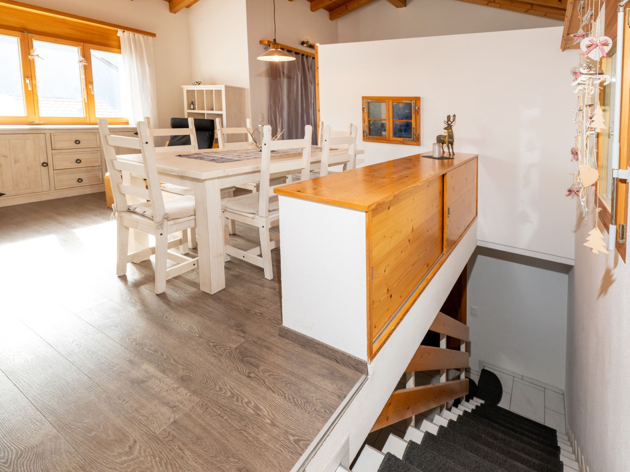 Ein Essbereich mit einem Holztisch und Stühlen, einem weißen Schrank und einer Treppe, die in eine obere Ebene führt.