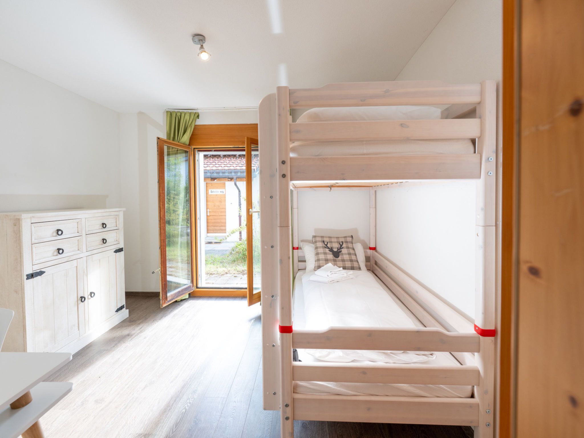 Ein Schlafraum mit Etagenbetten, einem Holzschrank und einer Tür zu einem Außenbereich.