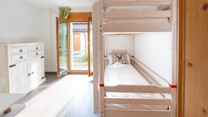 Een slaapkamer met stapelbedden, een houten garderobe en een deur naar een buitenruimte.