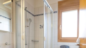 Een badkamer met een douchecabine van glas, een witte wastafel en een toilet.