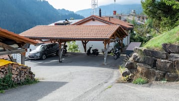 Un área de estacionamiento techada con un coche y una moto, rodeada por un paisaje montañoso.
