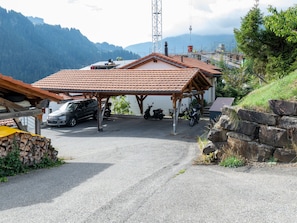 A covered parking area with a car and a scooter, surrounded by a mountainous landscape.