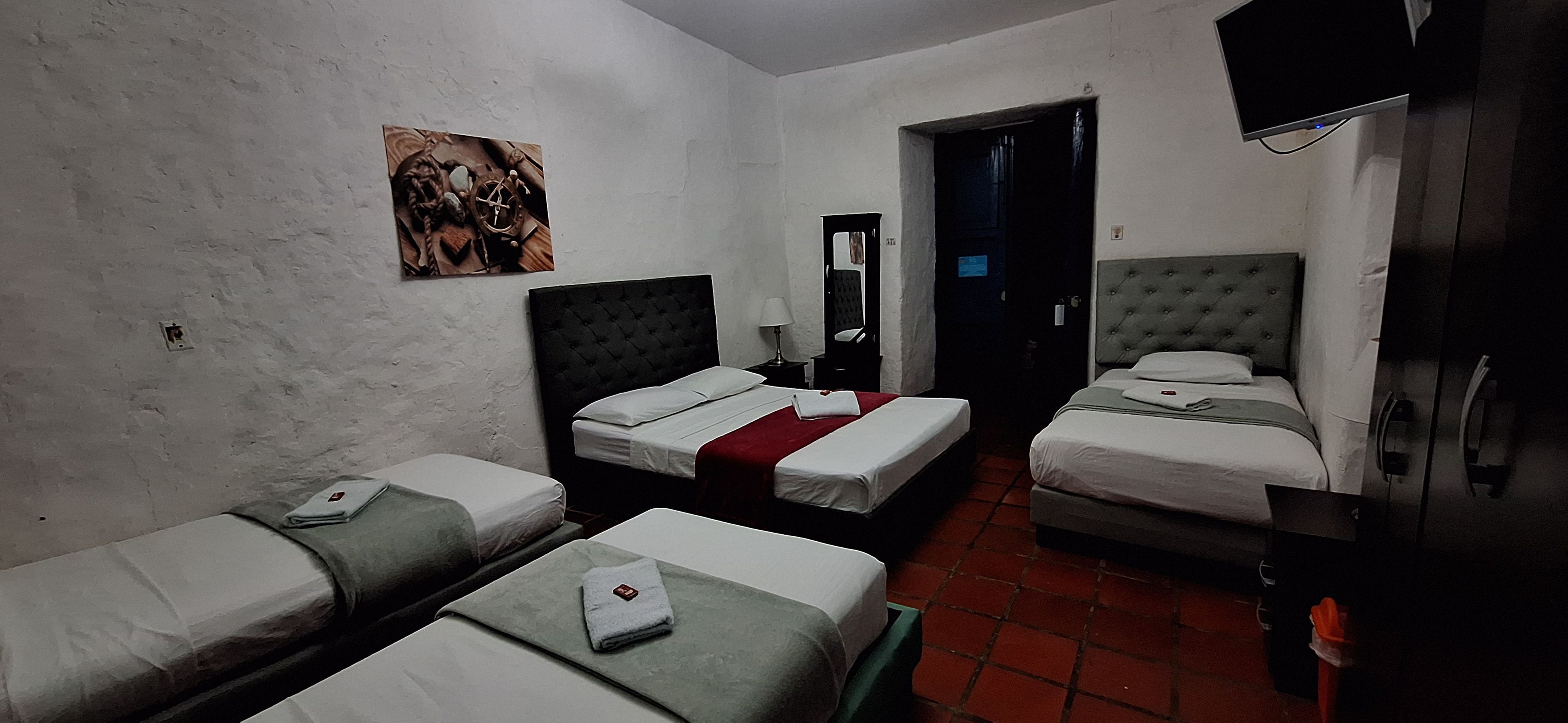 Habitación de hotel con dos camas individuales, una mesita, una silla, un armario y un cuadro en la pared.
