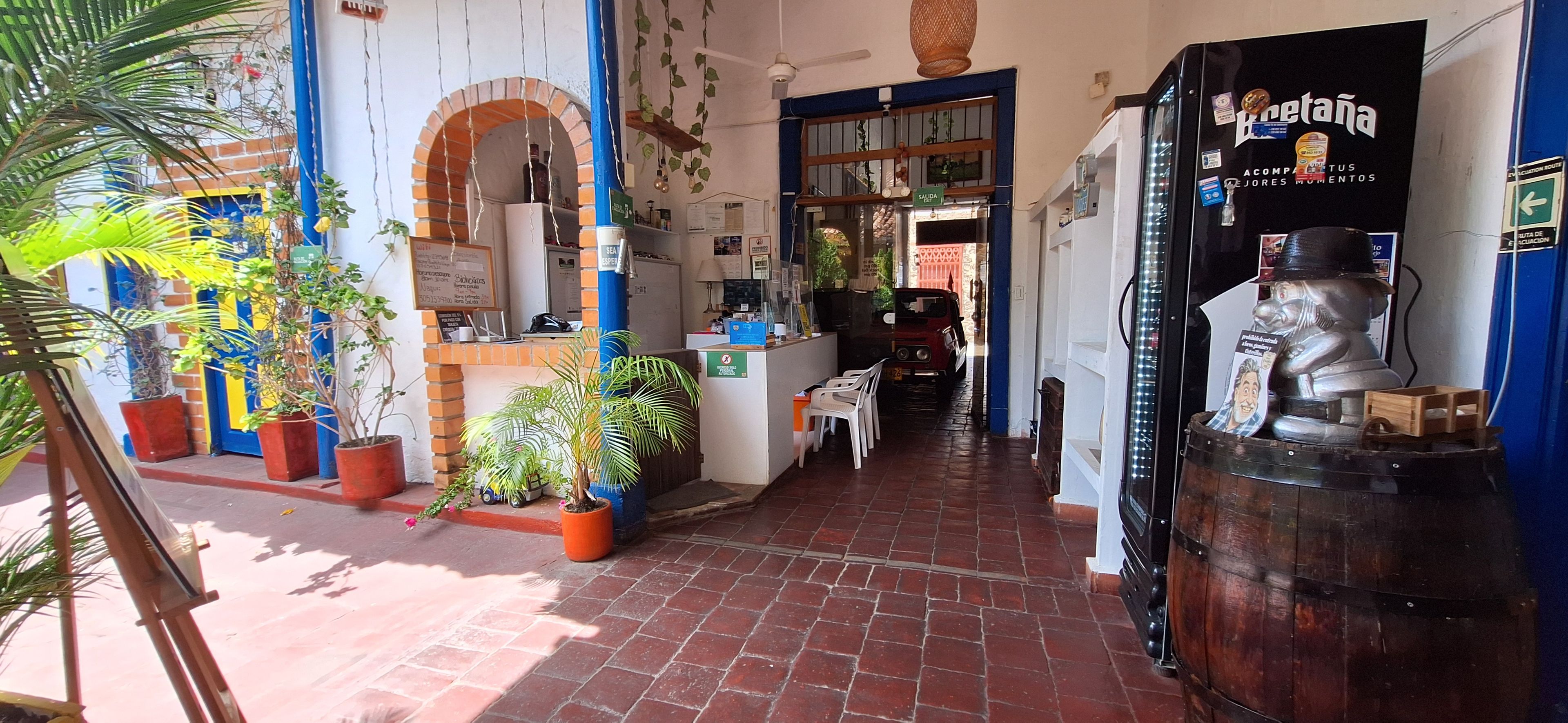 Un pasillo interior con piso de ladrillo, plantas en macetas, un mostrador con un letrero y una estatua.