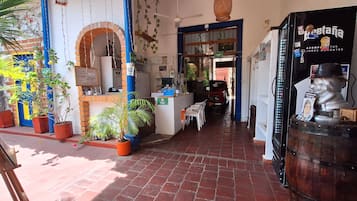 Un pasillo interior con piso de ladrillo, plantas en macetas, un mostrador con un letrero y una estatua.