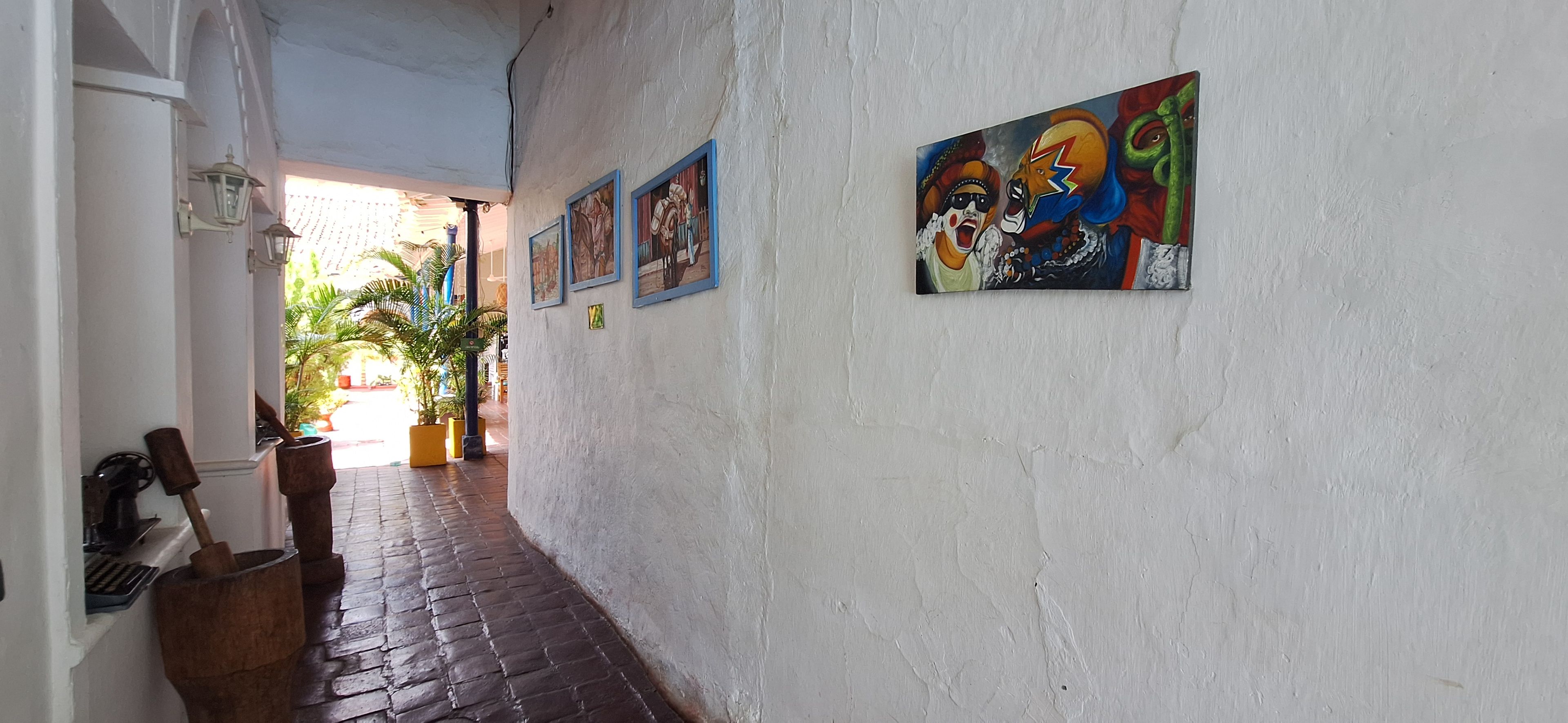 Un pasillo con piso de ladrillo, paredes blancas y varias obras de arte enmarcadas.