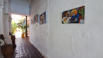 Un pasillo con piso de ladrillo, paredes blancas y varias obras de arte enmarcadas.