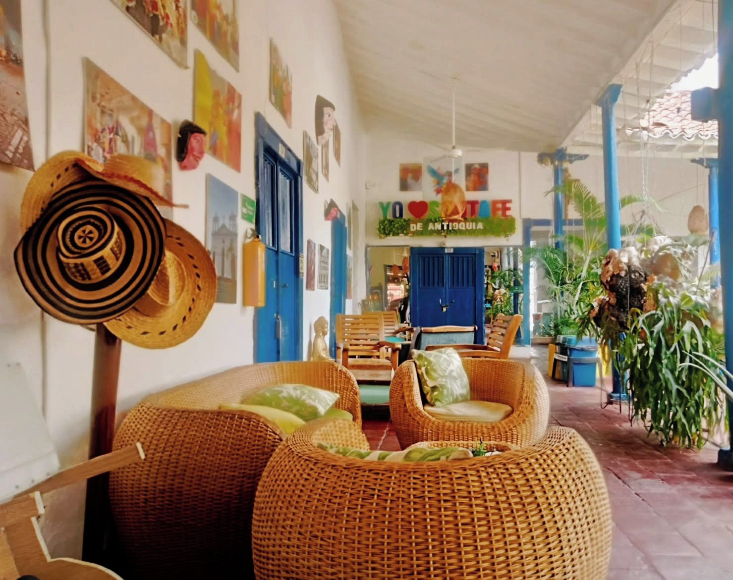 Een gezellig interieur met rieten meubels, een blauwe deur en een bord waarop staat 'YO LOVE ANTIOQUIA'.